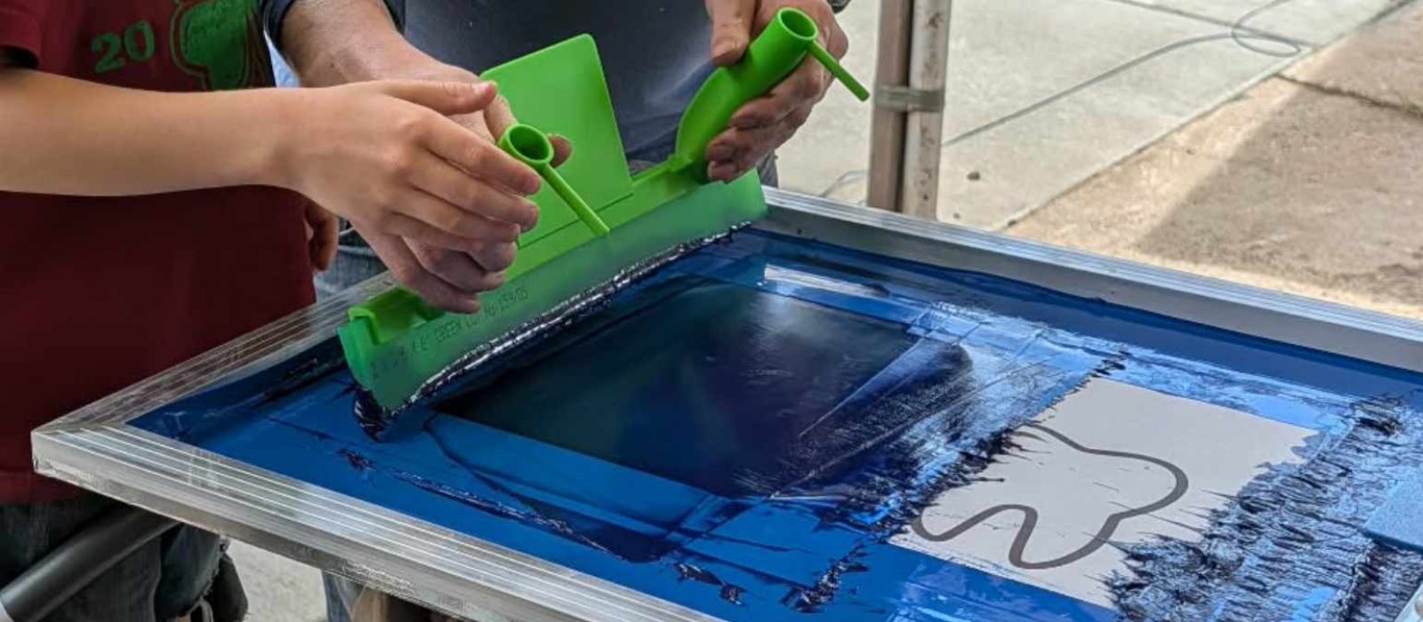 Guest pulling squeegee on press to book live screen printing in Ogden with Canyon Canvas